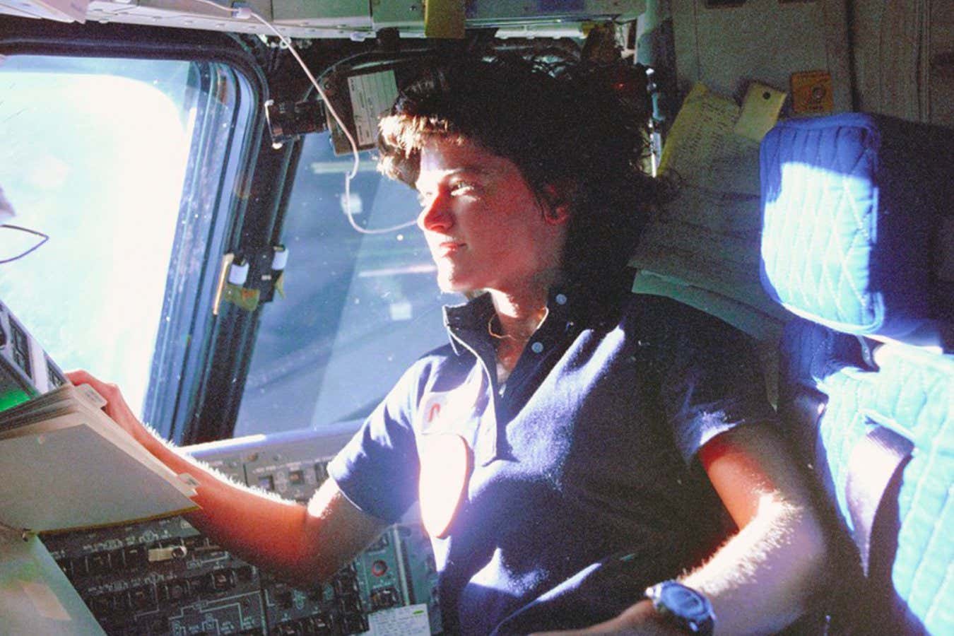 Astronaut Sally Ride, mission specialist on STS-7, monitors control panels from the pilot's chair on the Flight Deck. Floating in front of her is a flight procedures notebook. (Credit: NASA)