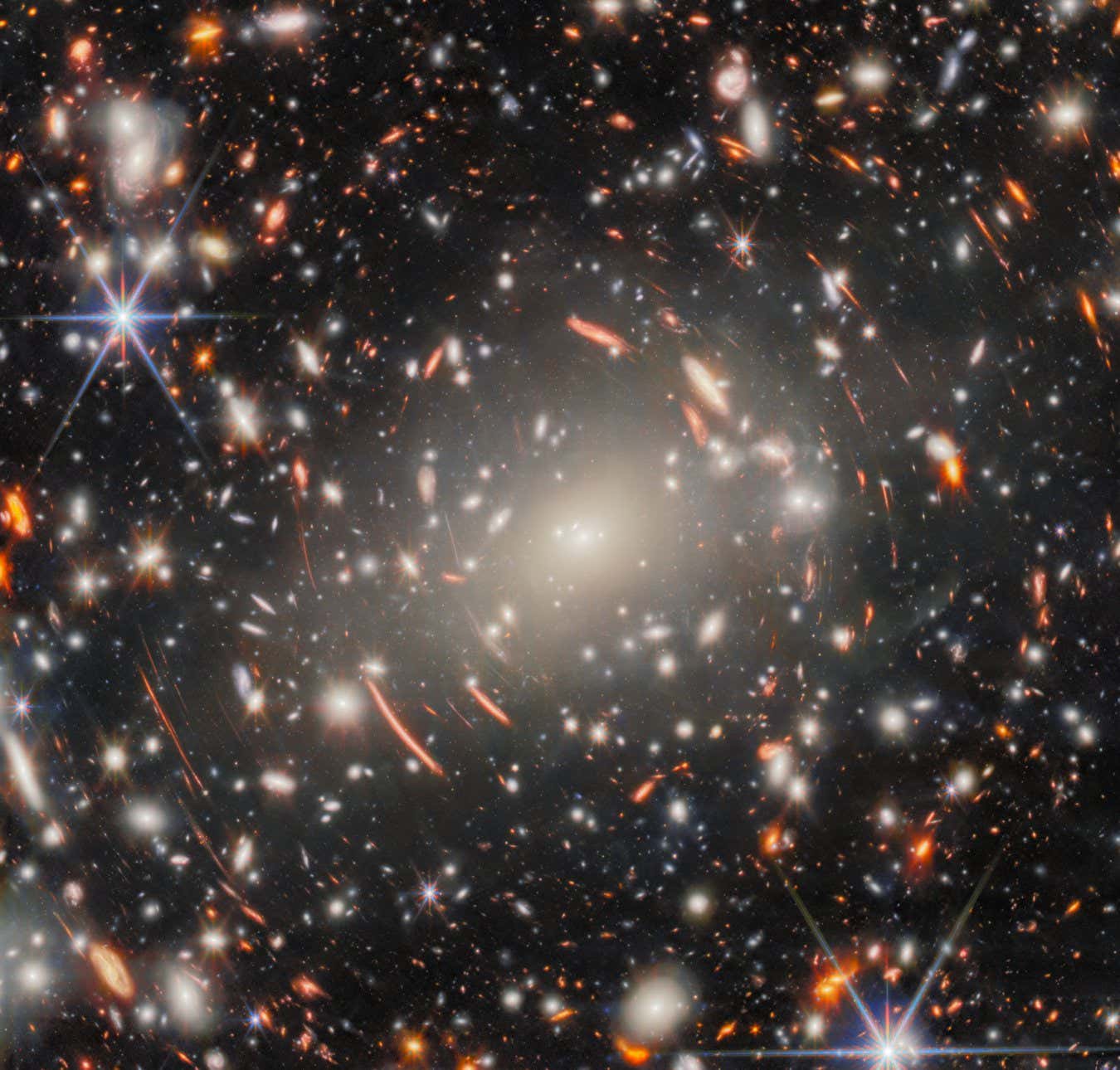 The eye is first drawn, in this new NASA/ESA/CSA James Webb Space Telescope Picture of the Month, to the central mega-monster that is galaxy cluster Abell S1063. This behemoth collection of galaxies, lying 4.5 billion light-years from Earth in the constellation Grus (the Crane), dominates the scene. Looking more closely, this dense collection of heavy galaxies is surrounded by glowing streaks of light, and these warped arcs are the true object of scientists??? interest: faint galaxies from the Universe???s distant past. Abell S1063 was previously observed by the NASA/ESA Hubble Space Telescope???s Frontier Fields programme. It is a strong gravitational lens: the galaxy cluster is so massive that the light of distant galaxies aligned behind it is bent around it, creating the warped arcs that we see here. Like a glass lens, it focuses the light from these faraway galaxies. The resulting images, albeit distorted, are both bright and magnified ??? enough to be observed and studied. This was the aim of Hubble???s observations, using the galaxy cluster as a magnifying glass to investigate the early Universe. The new imagery from Webb???s Near-Infrared Camera (NIRCam) takes this quest even further back in time. This image showcases an incredible forest of lensing arcs around Abell S1063, which reveal distorted background galaxies at a range of cosmic distances, along with a multitude of faint galaxies and previously unseen features. This image is what???s known as a deep field ??? a long exposure of a single area of the sky, collecting as much light as possible to draw out the most faint and distant galaxies that don???t appear in ordinary images. With 9 separate snapshots of different near-infrared wavelengths of light, totalling around 120 hours of observing time and aided by the magnifying effect of gravitational lensing, this is Webb???s deepest gaze on a single target to date. Focusing such observing power on a massive gravitational lens, like Abell S1063, therefore h